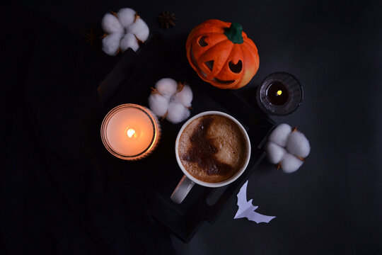 Halloween night celebration. Coffee on the tray with smiling pumpkin, burning candle, coconut flowers and bats on the black background. Halloween service. Trick or Treat! Eat, drink, and be scary. 