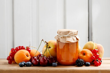 Jar with peach jam and fresh fruits on wooden table.