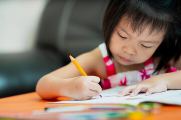 Selective focus of child hand coloring on workbook. Student kid learning. Kindergarten girl doing homework on orange table. Children aged 4-5 years old. Back to school.