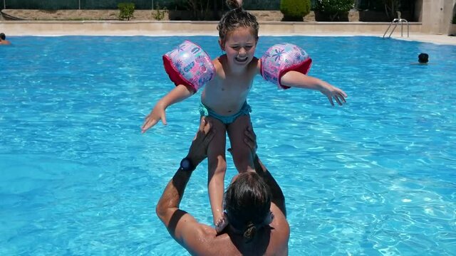 A cute little Caucasian girl standing on her father's shoulders and jumping into the swimming pool