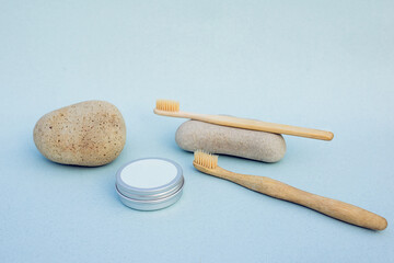 Two bamboo toothbrushes and round  silver can on light blue background. with grey natural stones. Organic toothpowder and zero waste brushes concept