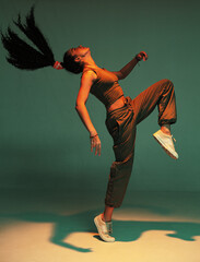 Dancing athletic mixed race girl performing expressive fiery hip hop or ethnic modern dance in colourful studio light