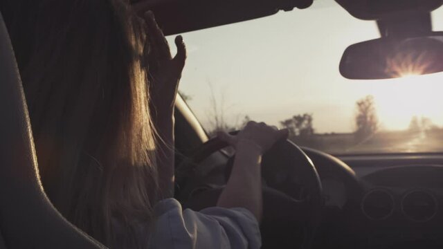 A young girl driving a convertible starts moving. The beginning of the journey. Woman driving a car. Holds the steering wheel with his hands. Roadtrip on the highway. Hair in the wind in slow motion.