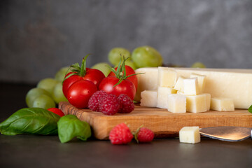 tomatoes, cheese, basil, raspberries and grapes on an olive board on a dark background