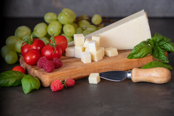 tomatoes, cheese, basil, raspberries and grapes on an olive board on a dark background