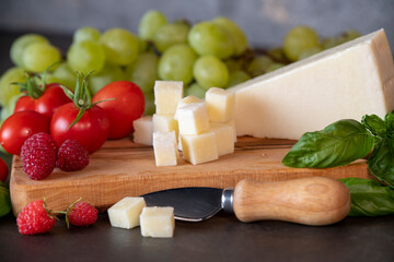 tomatoes, cheese, basil, raspberries and grapes on an olive board on a dark background