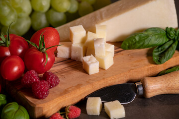 tomatoes, cheese, basil, raspberries and grapes on an olive board on a dark background