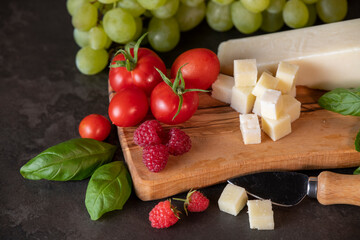 tomatoes, cheese, basil, raspberries and grapes on an olive board on a dark background