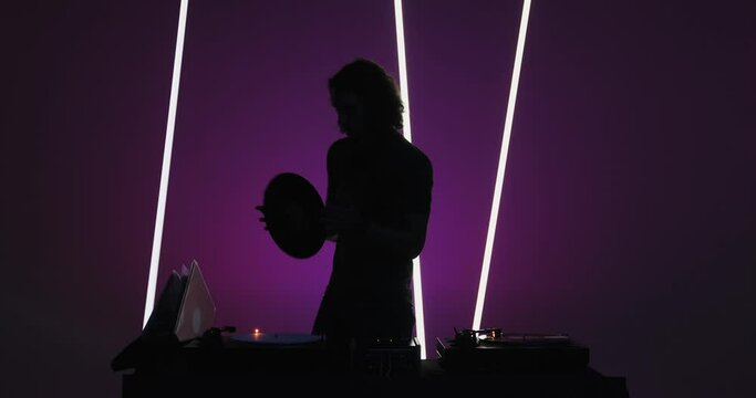Silhouette of cool modern male deejay playing vinyls at dj console in nightclub. Nightlife and partying