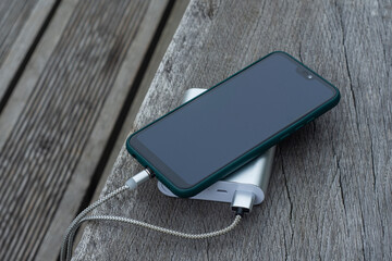 Power Bank charges a smartphone on a wooden bench in the park.