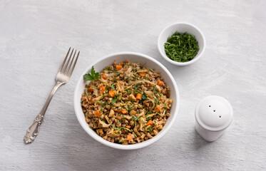 Delicious vegetarian buckwheat with cabbage, carrots, onions, nuts and herbs on a light gray textured background