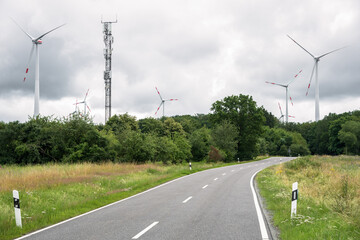 Deserted country road running through a wind farm on a cloudy summer day