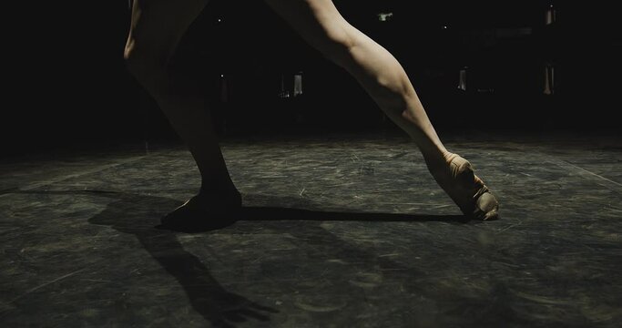 Graceful modern ballet female dancer performing choreography on theatre stage with dramatic lighting. Close up
