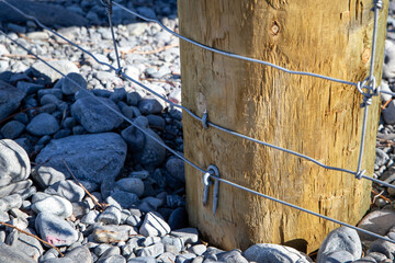 Close up of components of a post and netting farm fence along the border of the farm and river bed,...