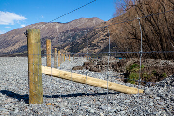 New post and netting fence dividing the farm boundary from the river bed  in the high country,...