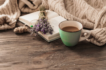 A cup of coffee on a wooden table, an open book and a warm sweater on the background of a bouquet...