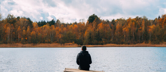 Rear view, a man on a wooden bridge by the lake against the background of an autumn forest.