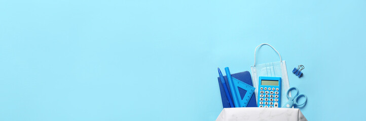 Pencil case with stationery and medical mask on color background with space for text