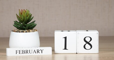 Wooden calendar with an important event for february 18, a woman's hand sets the date on the calendar. Winter season.