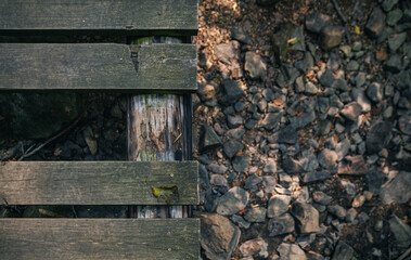 Looking down at footbridge with a board missing. Dry creek bed stones underneath. Nature and hiking trail background.