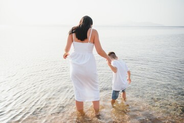 Happy mother and son walk along the ocean beach having great family time on vacation on Pandawa Beach, Bali. Paradise, travel, vacation concept