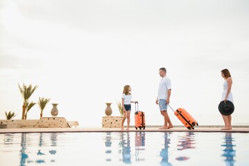 young family with suitcases walking to hotel building with beautiful swimming pool. traveling and relaxing time concept.