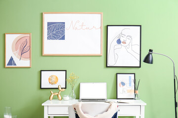 Modern workplace with laptop and pictures near color wall