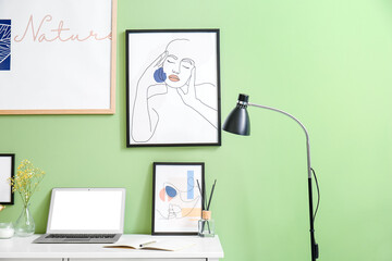 Modern workplace with laptop and pictures near color wall