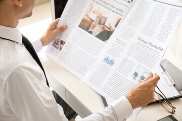 Young businessman reading newspaper in office, closeup