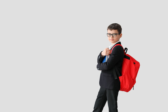 Little schoolboy with books on light background