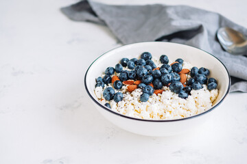 Crumbly curd with blueberries, almonds and chia seeds in white bowl on the table with copy space.