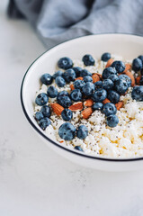Crumbly curd with blueberries, almonds and chia seeds in white bowl on the table.