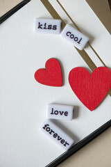 the expression "kiss cool, love forever" with two red hearts on fancy paper