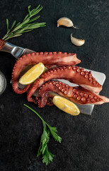 Boiled octopus tentacles on a knife on a stone background