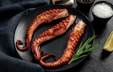 grilled octopus tentacles, on a dark plate on a stone background