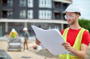 Engineer in a vest and hardhat studying a building plan