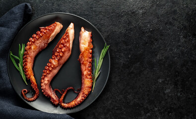 grilled octopus tentacles, on a dark plate on a stone background with copy space for your text