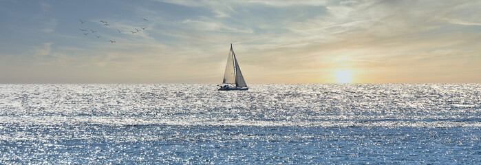 Small sailboat sailing through a silver sea at sunrise