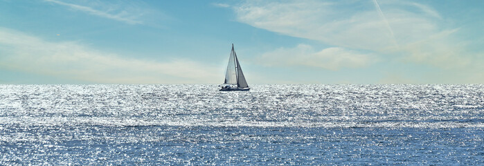 Small sailboat sailing through a silver sea in a sunny day 