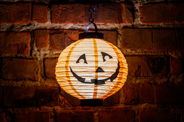 Smiling glowing jack-o-lantern hanging on old red brick wall at night. Halloween decoration concept