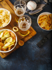 Beer in glasses and snacks - chips, onion rings, remote control. In the background is a baseball glove. Sports fans, group of friends, family, leisure. Watching sports matches on TV.