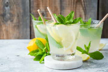 Two glass with lemonade or mojito cocktail with lemon and mint, cold refreshing drink or beverage with ice on rustic blue background. Copy space