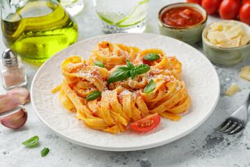 Tasty appetizing classic italian tagliatelle pasta with tomato sauce, cheese parmesan and basil on plate on light table. View from above, horizontal