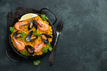 Traditional spanish seafood paella in pan with chickpeas, shrimps, mussels, squid on black concrete background. Top view with copy space