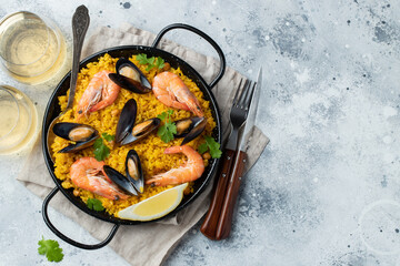 Traditional spanish seafood paella in pan with chickpeas, shrimps, mussels, squid on light grey concrete background. Top view with copy space