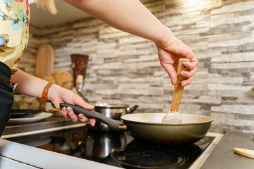 Close up on hands of unknown caucasian woman cooking at home in the kitchen holding pan