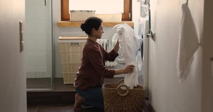 Indian housewife young woman do housework, busy in regular housekeeping work put bath towels into washing machine, turns on modern washer-dryer appliance in cozy laundry room. Household chores concept