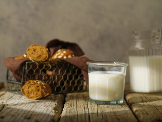 Black bread in a basket on a brown napkin and milk In a glass and a jug. Wooden texture. Grey...