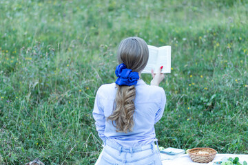 Back view of a blonde female with a beautiful trendy scrunchy on her hand reading a book