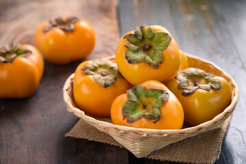 Ripe persimmon fruit in a bamboo basket on wooden background